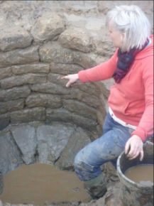 Archaeologist pointing at well at end of its investigation showing stone base and coursed stone lining (Source: OnSite Archaeology).